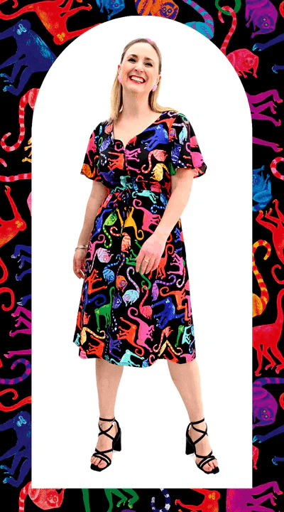 Brightly patterned dress featuring multi-colored abstract animal shapes, worn by a woman against a background that mirrors the vibrant theme, combining playful art with fashion. Designed by Australian designer brand Streborclothing. Slow fashion gift.