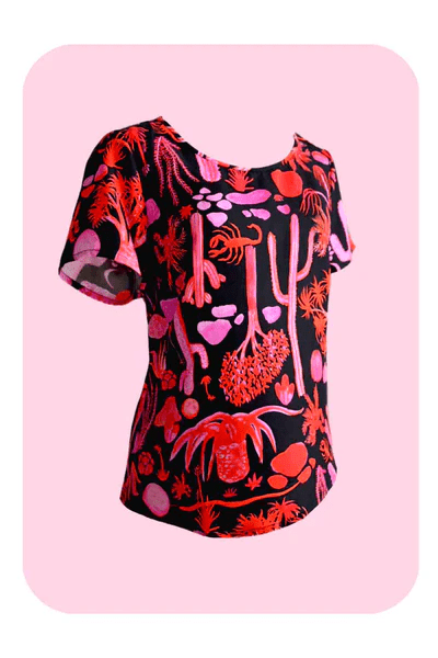 a vibrant black top with a pink and orange desert-themed print, posed against a similarly themed background, emphasizing the bold, artistic nature of Strebor's style. Designed by Australian designer brand Streborclothing.