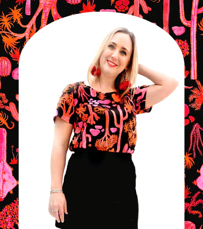 Woman wearing a vibrant black top with a pink and orange desert-themed print, posed against a similarly themed background, emphasizing the bold, artistic nature of Strebor's style. Designed by Australian designer brand Streborclothing.