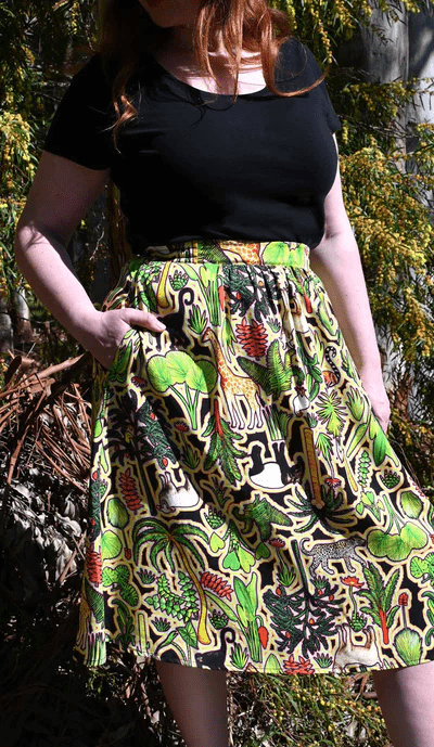 This top showcases a complex pattern with elements of flora, including leaves, flowers, and abstract natural shapes in shades of green, red, and yellow. The design appears dense and rich, resembling an intricate forest scene. Designed by Australian designer brand Streborclothing.